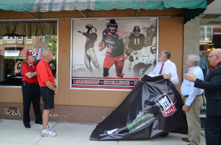 NIU President Doug Baker (right) unveils the NIU quarterback greats window Tuesday outside of the Lincoln Inn, 240 E. Lincoln Highway. This is the second year the city has partnered with NIU to honor Huskies players and athletics through window displays.NIU President Doug Baker (right) unveils the NIU quarterback greats window Tuesday outside of the Lincoln Inn, 240E. Lincoln Highway. This is the second year the city has partnered with NIU to honor Huskies players and athleticsthrough window display
