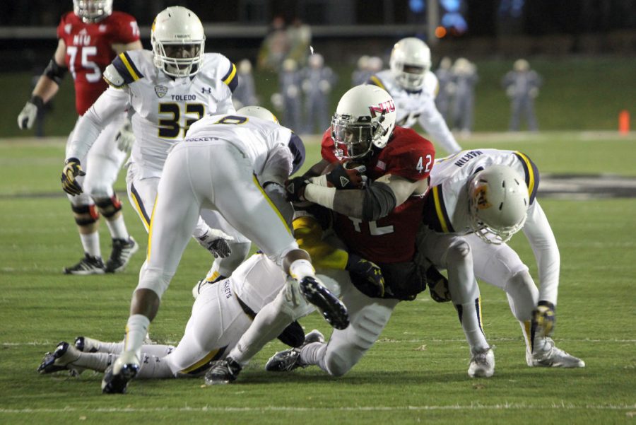 Redshirt senior tailback Cameron Stingily (42) is tackled by Toledo players Tuesday at Huskie stadium. NIU won the matchup, 27-24. Stingily scored two touchdowns in the second half of the game.