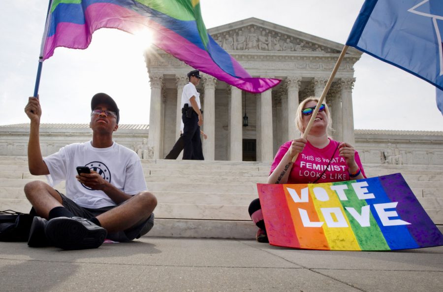 Carlos McKnight, 17, of Washington (left) and Katherine Nicole Struck, 25, of Frederick, Md., hold flags in support of gay marriage as security walks behind outside of the Supreme Court in Washington on Friday. 
