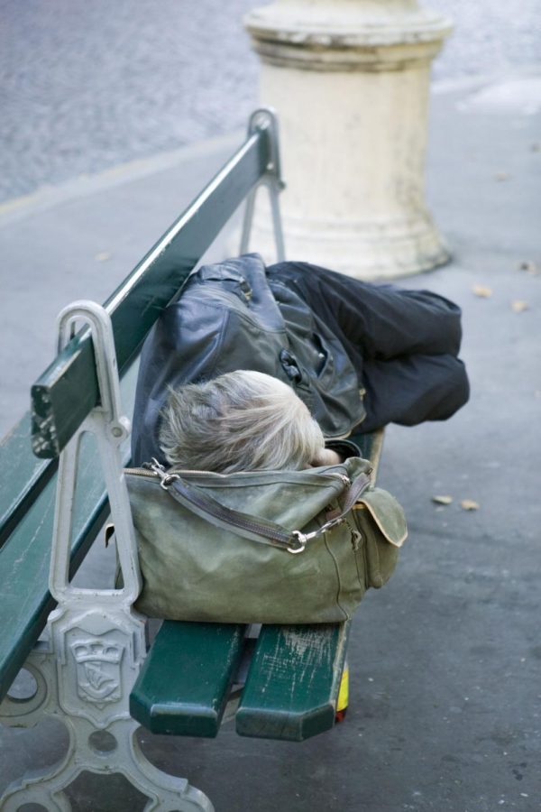A person sleeps on a sidewalk bench.