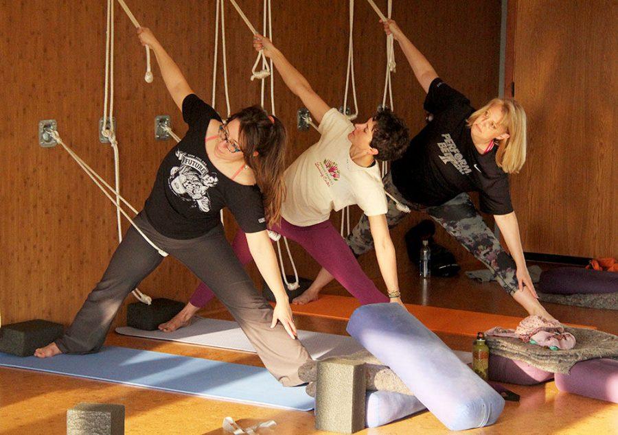 (From left) Rockford community members Allison Hollman, Nicole Messink and Kim White stand in the triangle pose while reaching toward their ankles to stretch their legs and obliques. 