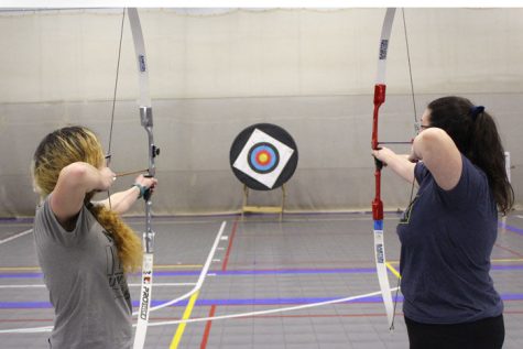 Freshman accounting major Antonia Mendez (left) and junior elementary education major Amanda Childers draw back their bows and aim at a target during the archery meeting Monday.
