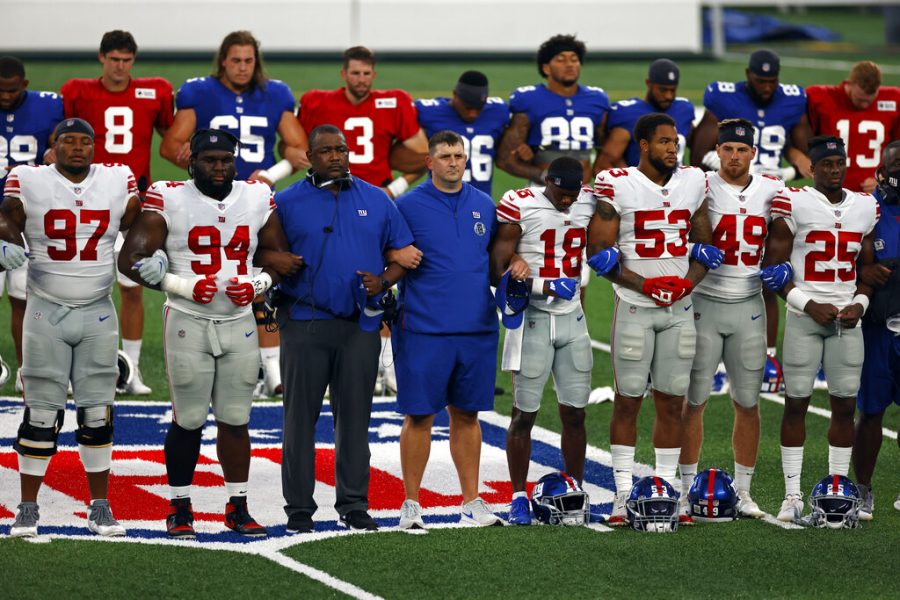 New York Giants head coach Joe Judge, center, stands with arms linked with his players to make a social injustice statement prior to their scrimmage at the NFL football team's training camp in East Rutherford, N.J., Friday, Aug. 28, 2020. A long-time advocate of the right to protest for social change and equality, New York Giants co-owner John Mara admits he was stunned listening to his players talk about their experiences with police and authorities in the wake of the death George Floyd in June. 