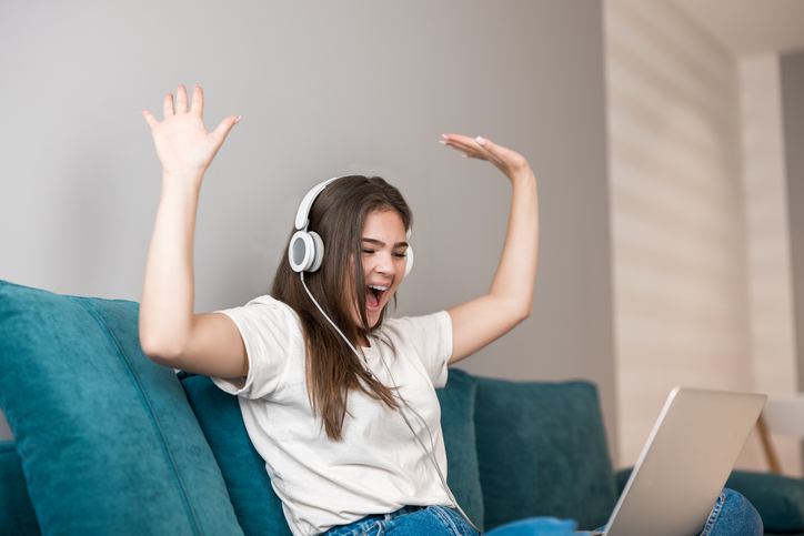 young woman in headphones listening to music from laptop on the sofa in the living room.