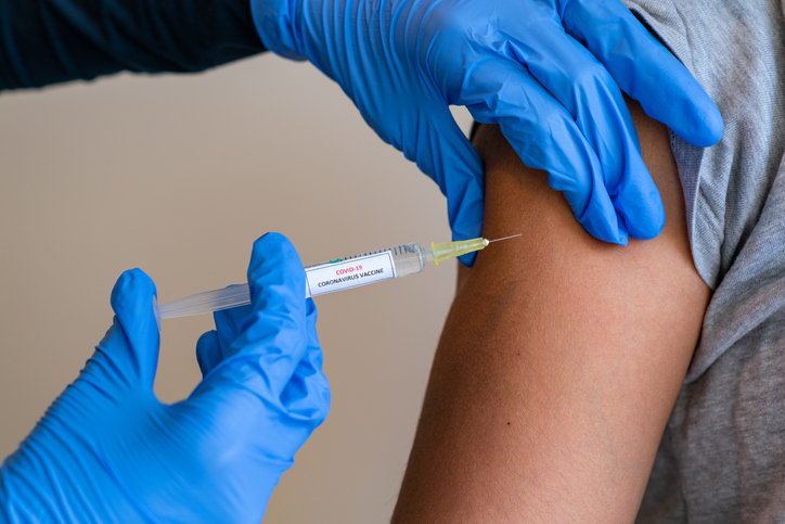 A+clinician+uses+a+syringe+to+inject+a++COVD-19+vaccine+into+a+patient.