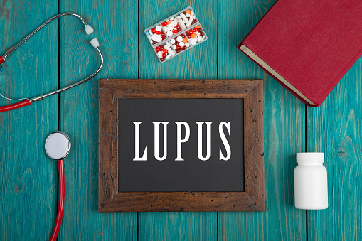 Blackboard with text Lupus, book, pills and stethoscope on blue wooden background.