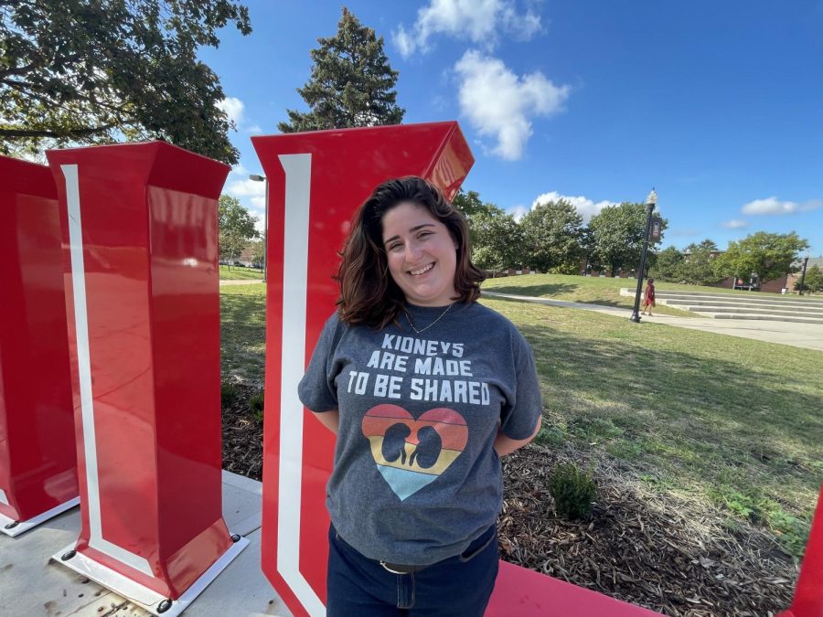 Amanda McGovern, a junior communicative disorders major stands in front of an NIU sign wearing a shirt that says kidneys are meant to be shared.