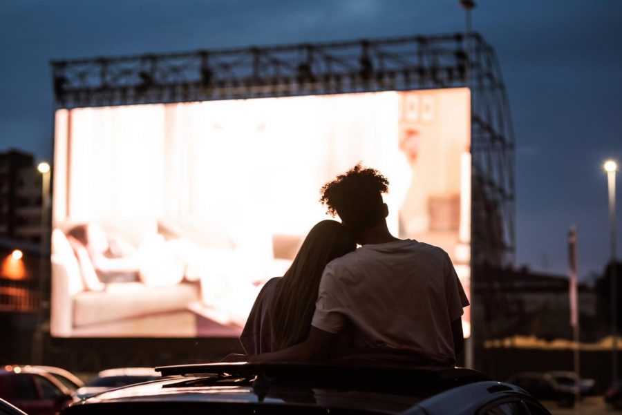 Silhouetted view of a young couple, embracing, spending time together and sitting in the car while watching a movie at a drive-in cinema.