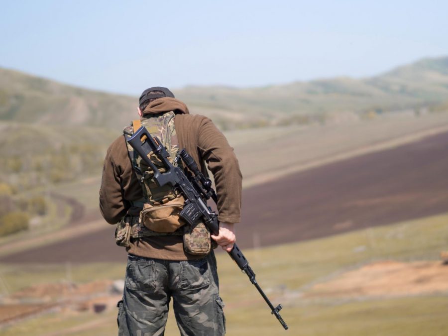A man stands outside with a gun strapped onto his back. 
