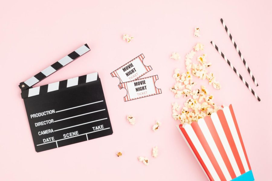 Movie clapperboard, tickets and popcorn over pink background.