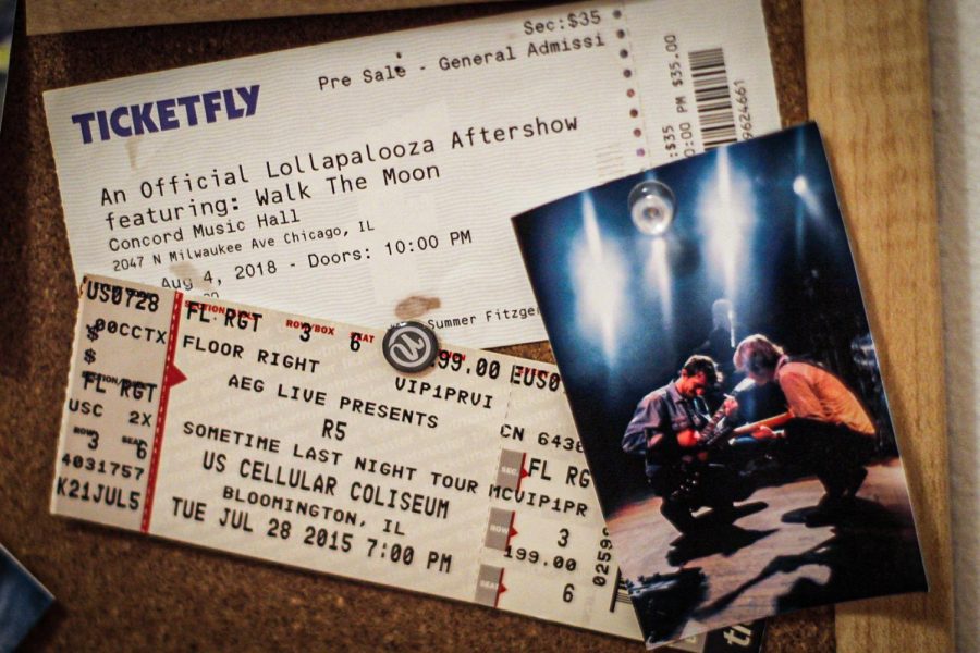 A set of old concert tickets rests on a bulletin board alongside a photograph. The ticket stubs are for Walk the Moon in 2018 and The Driver Era (formerly R5) in 2015. The photograph is from The Driver Era in 2019.