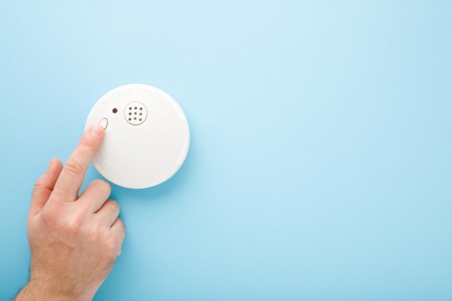 A smoke alarm being tested, hanging on a blue wall. (Photo courtesy of Getty Images)