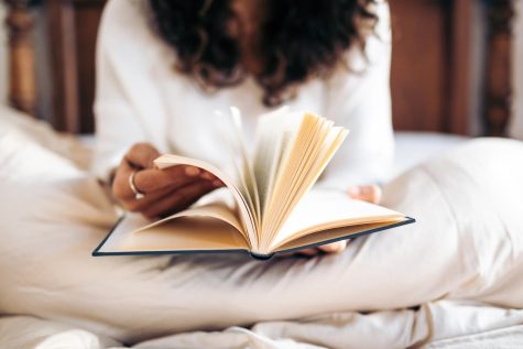 A young woman flips through the pages of a book while sitting in bed. 