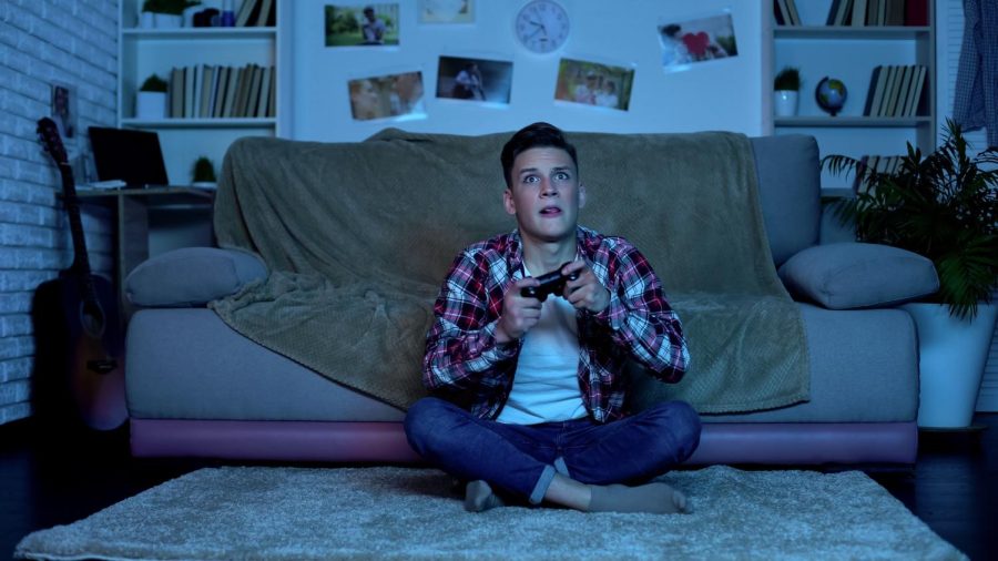 A man sitting on the floor playing video games with the blue light from the tv on his face.