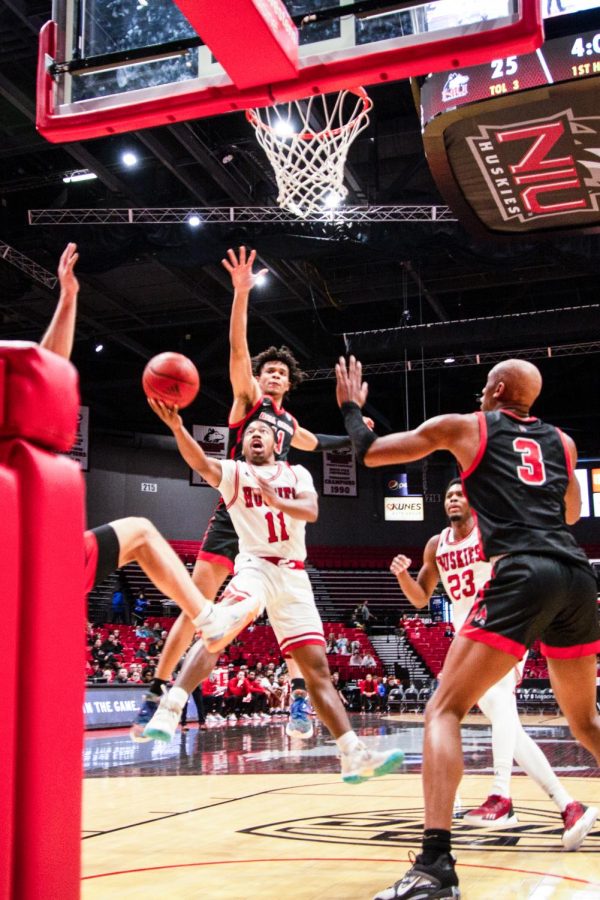 David Coit (11) shoots against Ball State sophomore forward Basheer Jihad (11) and redshirt sophomore forward Mickey Pearson Jr. (3) during the first half of an NCAA basketball game Jan. 28 at the Convocation Center in DeKalb. (Mingda Wu | Northern Star)