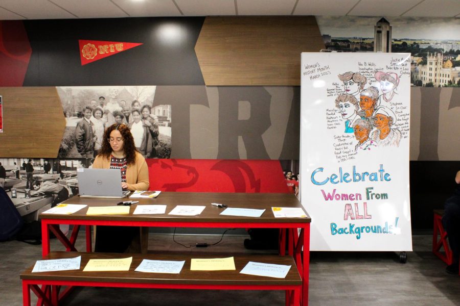 GSRC Associate Director Ariel Owens sits at the “Women’s History is…” photo series table, where the GSRC provided posters for female students to share their views on Women’s History Month and take a picture with the poster Thursday in Holmes Student Center. (Nyla Owens| Northern Star)