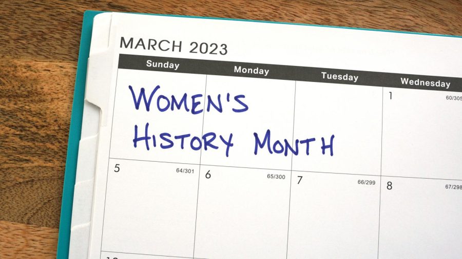 Womens History Month written on a March 2023 calendar in front of a wood background. 