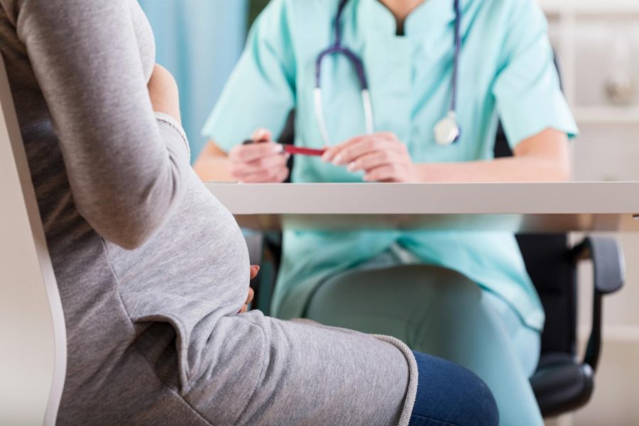 A pregnant woman holding her belly while talking to a doctor. WeCare4NIU is a outreach organization working with the We Care Clinic Pregnancy Clinic in downtown DeKalb. 