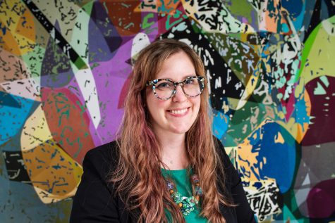 Associate professor and head of the photography department at NIU, Jessica Labatte, standing in front of a vibrant wall mural. Labatte has been selected to be the next Director of the NIU School of Art and Design, beginning in July. (Courtesy of Amy Fleming)