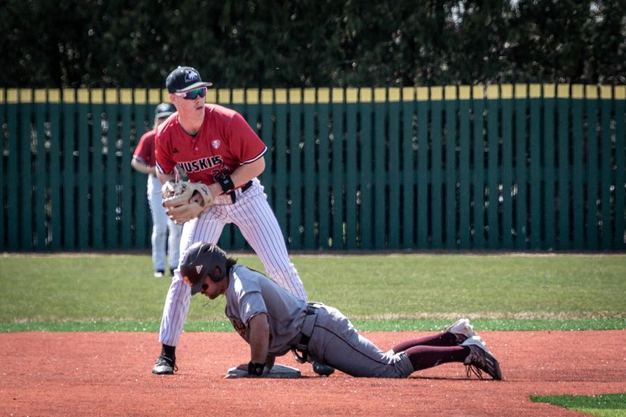 NIU junior second baseman Aaron Harper (22) retrieves the ball from his glove as a CMU runner lifts himself up from the base. (Mingda Wu | Northern Star)