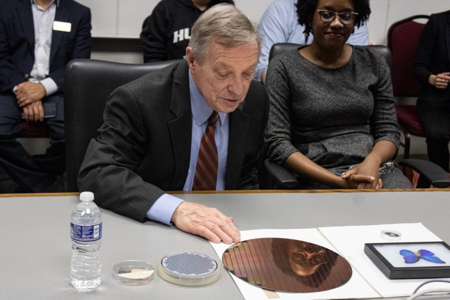 Durbin (left) looks at a silicon wafer on the table as the microchip fabrication is explained briefly during the meeting Wednesday on the third floor of the CEET. (Sean Reed | Northern Star)