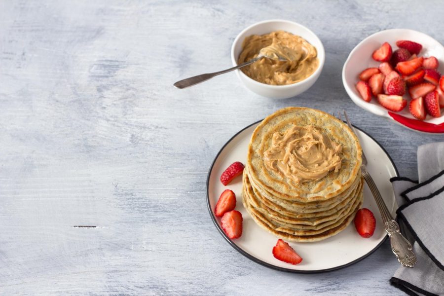 A plate of pancakes with peanut butter and strawberries sitting on a table. Peanut butter with pancakes is a great way to improve the taste and texture of pancakes. 