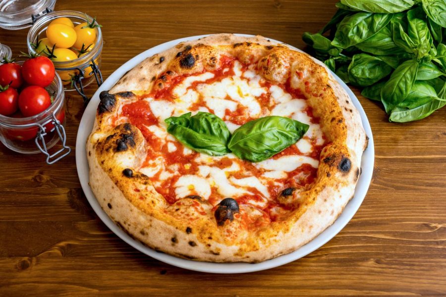 A Margherita pizza on a plate with tomatoes and basil besides it. Senior Columnist Angelina Padilla-Tompkins debates which pizza place is the best. 