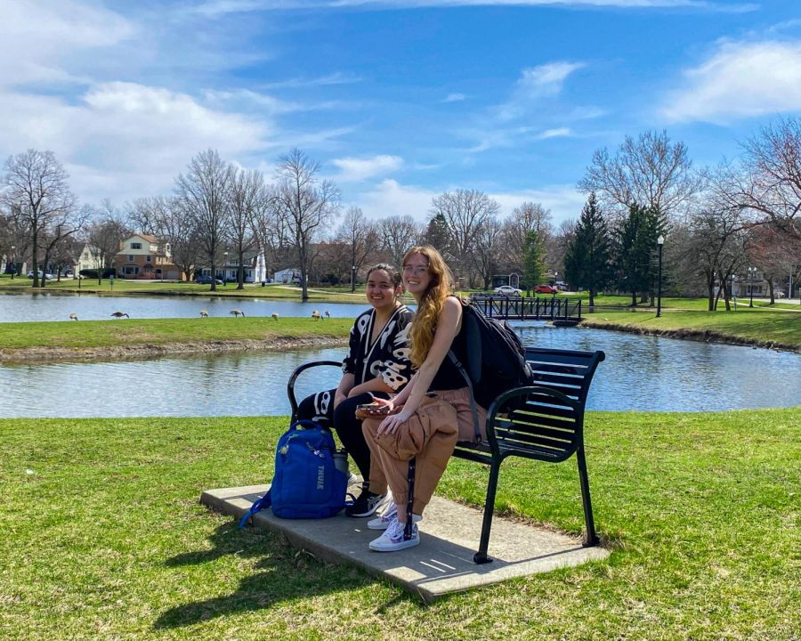 Jesenia Solano (left), a freshman electrical engineering major, and Sydney Fields, a sophomore double majoring in biology and psychology, sit on a bench after hunting around the East Lagoon for the Northern Star paperweight on Tuesday. (Sean Reed | Northern Star)