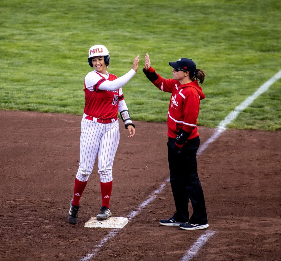 Senior utility player Sam Mallinder (18) high-fives the first base coach after hitting a single that drove in a run during the third inning. The Huskies lost the game 7-6. (Tim Dodge | Northern Star) 