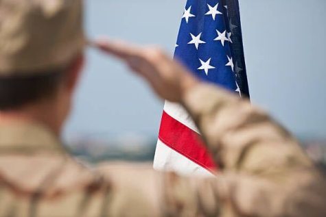 An out of focus soldier salutes an American flag. Graduating veteran students find that the military has offered them worthwhile experiences during the college process. (Getty Image)