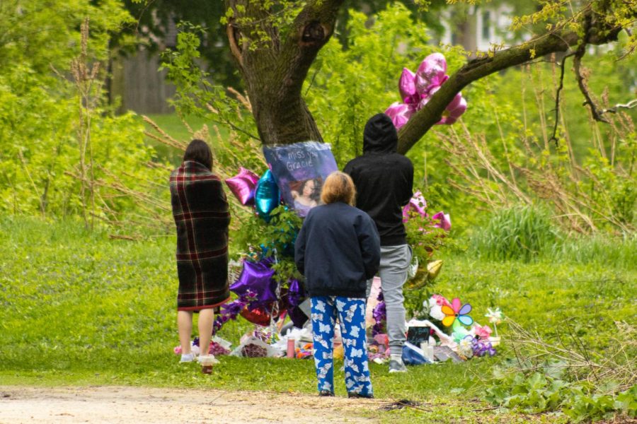 Three attendees stand around a memorial, which features a poster on the tree with a photo of Gracie Sasso-Cleveland and the words “We miss you Gracie.” (Sean Reed | Northern Star)