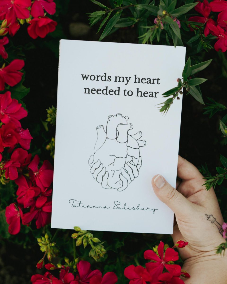 NIU alum Tatianna Salisburys debut book is held surrounded by red flowers. Salisburys debut poetry collection can be purchased from Amazon, Walmart or Barnes & Noble. (Courtesy of Tatianna Salisbury)