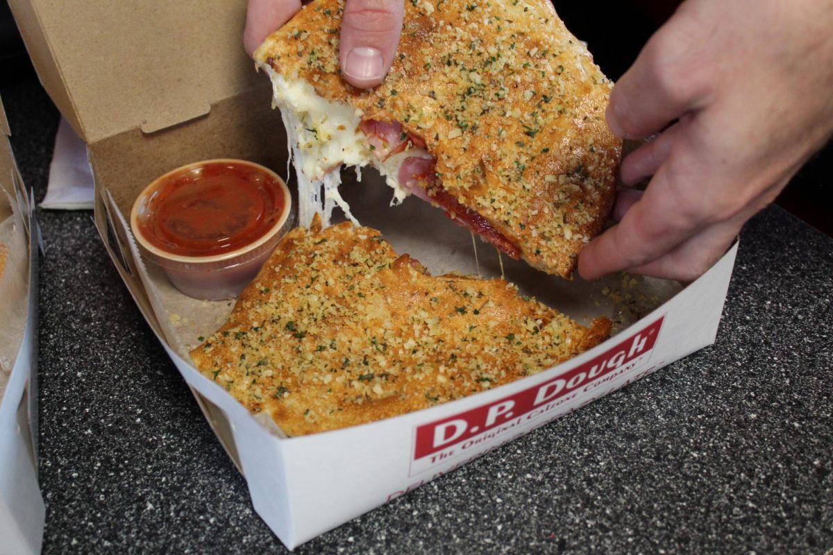 A calzone from D.P. Dough is ripped in two and has cheese pulling between halves. D.P. Dough, a new restaurant in DeKalb, had a soft opening on Tuesday. (Michael Mollsen | Northern Star)