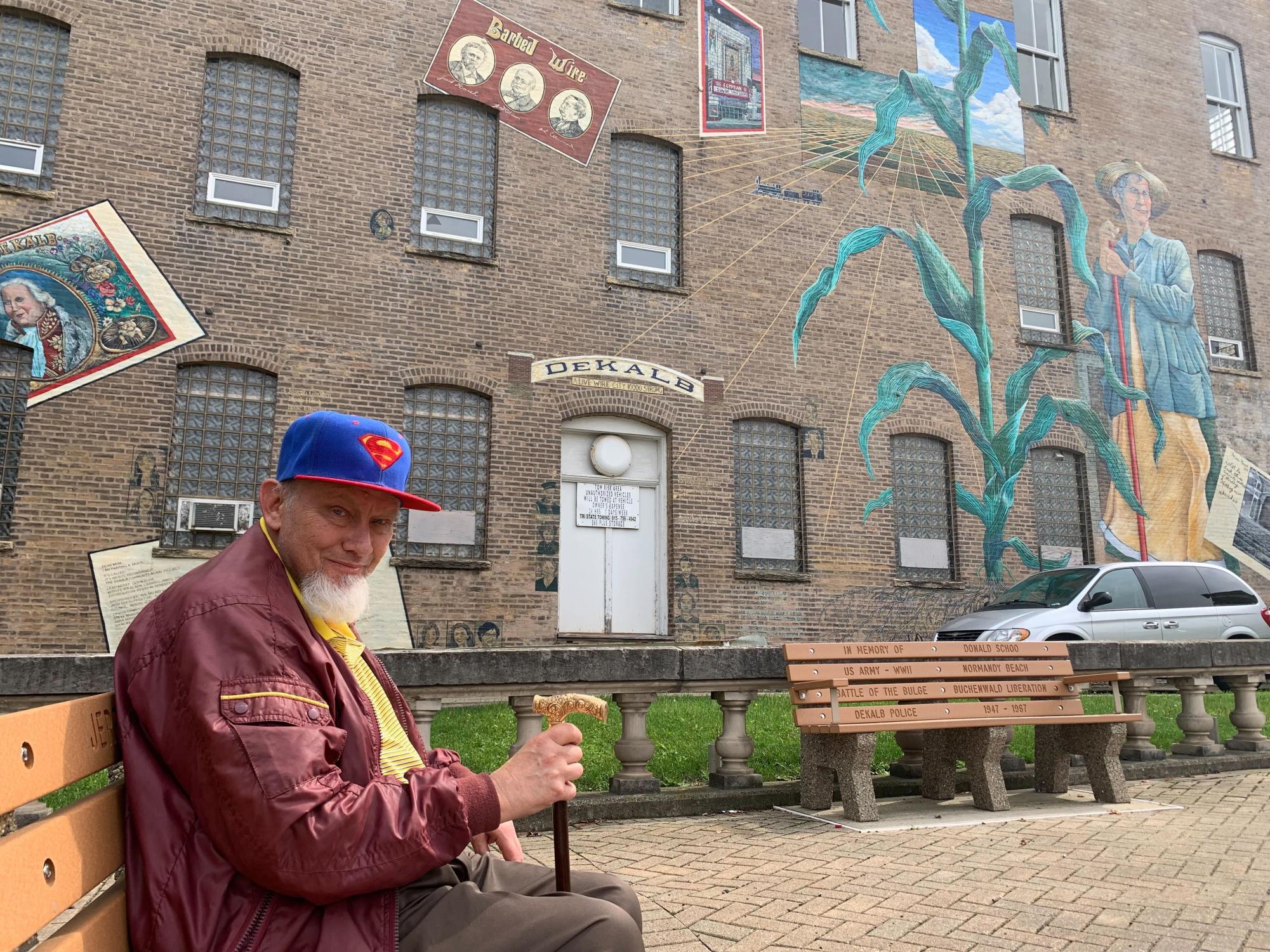 Stephen J. Bigolin sits on a park bench on Sept. 20 at Memorial Park in front of the mural facing Lincoln Highway. Bigolin has supported and discovered DeKalb’s local history since he moved to DeKalb in 1967. (Rachel Cormier | Northern Star)