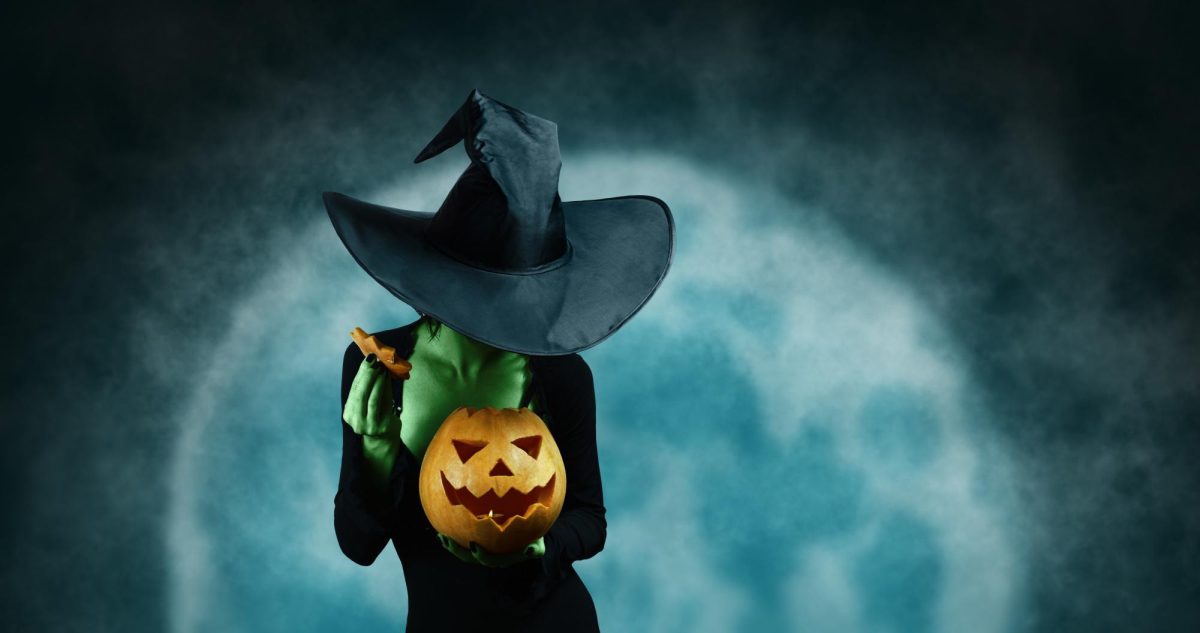 A woman dressed as a green witch holds a jack-o’-lantern. A person is never too old to celebrate Halloween. (Courtesy of Getty Images)