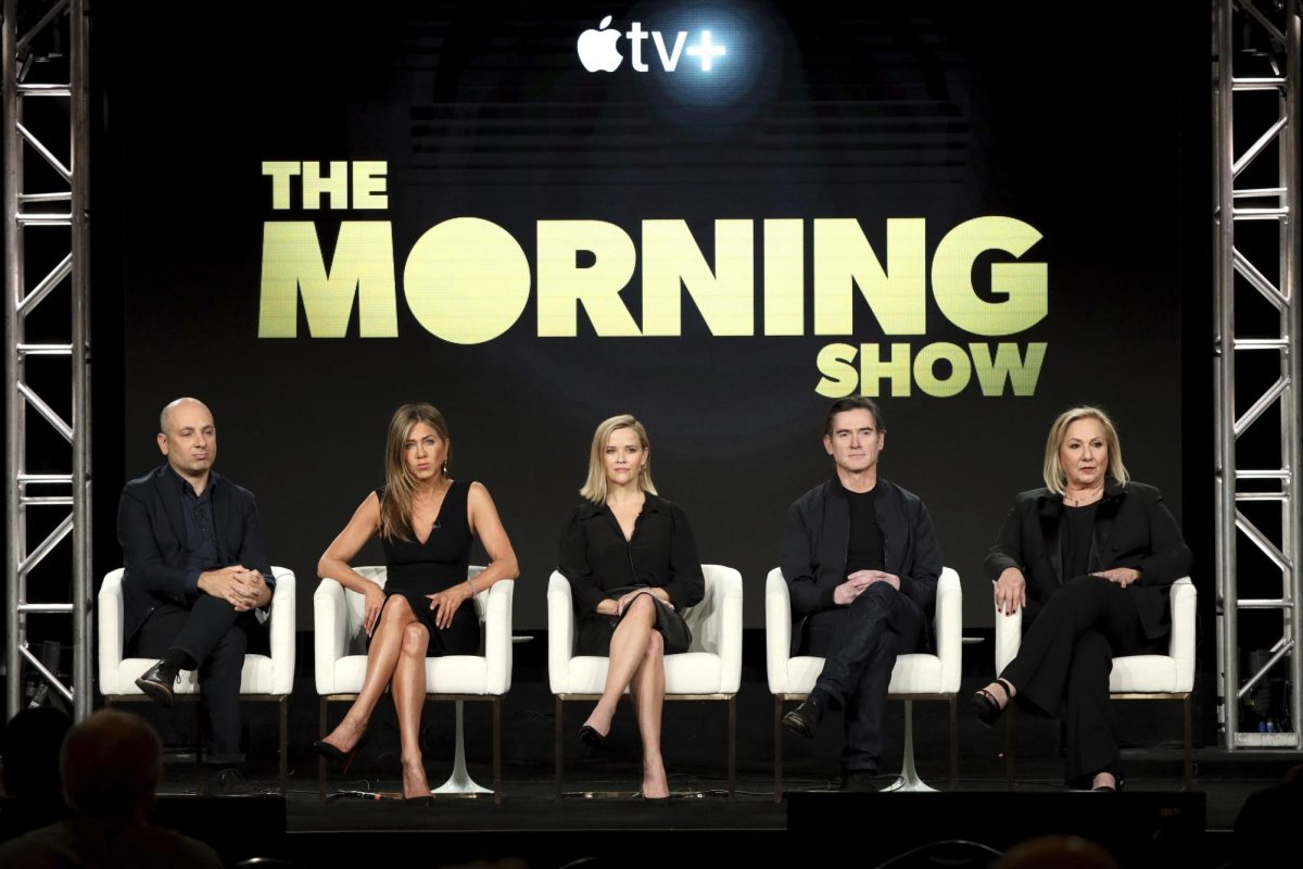 (From left) Michael Ellenberg, Jennifer Aniston, Reese Witherspoon, Billy Crudup and Mimi Leder sitting at a panel in 2020 with the name of their series, The Morning Show, in yellow letters behind them. The Apple+ show is on their third season with episodes releasing weekly. (Willy Sanjuan/Invision/AP)