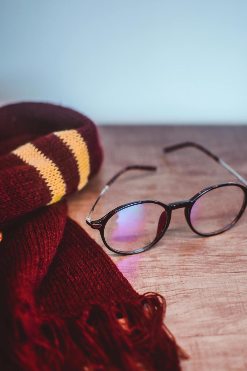 A Gryffindor scarf and round glasses lay on a table. Which Harry Potter Defence Against the Dark Arts professor is your favorite? (Vinícius Vieira ft | Pexels)
