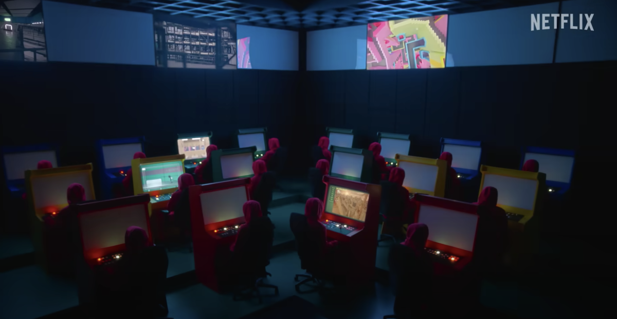 Eighteen individuals in red hoods sit at multicolored gaming desks. Squid Game: The Challenge is a reality series based on Squid Games and will release on Netflix Nov. 22. (Courtesy of YouTube)