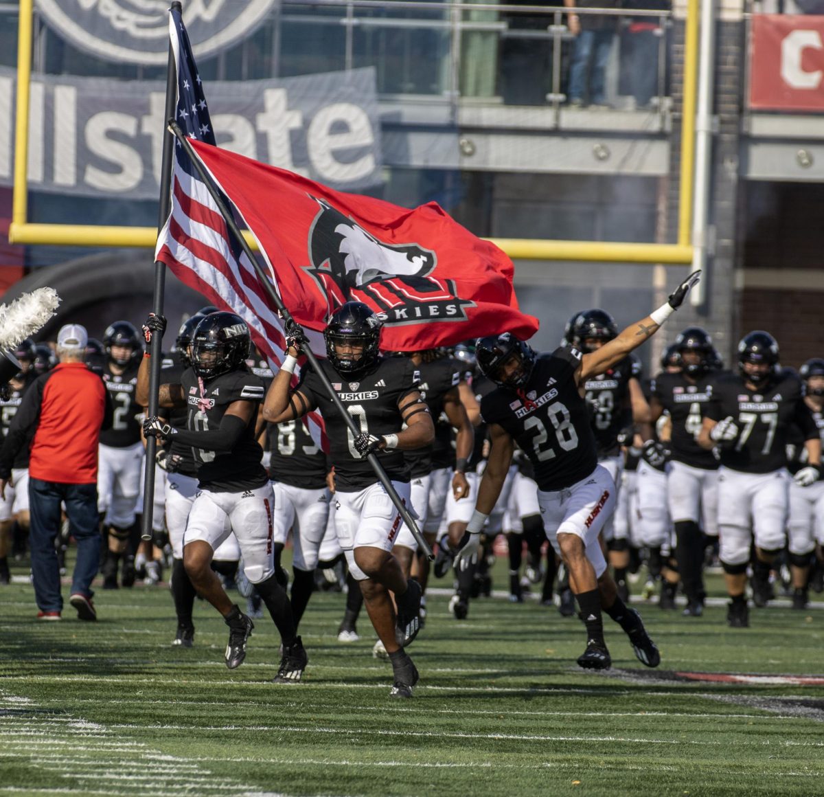 Redshirt senior Tyler Jackson (0) holds the NIU flag as he leads the team onto the Huskie Stadium field on Oct. 21. The Huskies will take on Arkansas State in the Camellia Bowl on Dec. 23. (Tim Dodge | Northern Star)