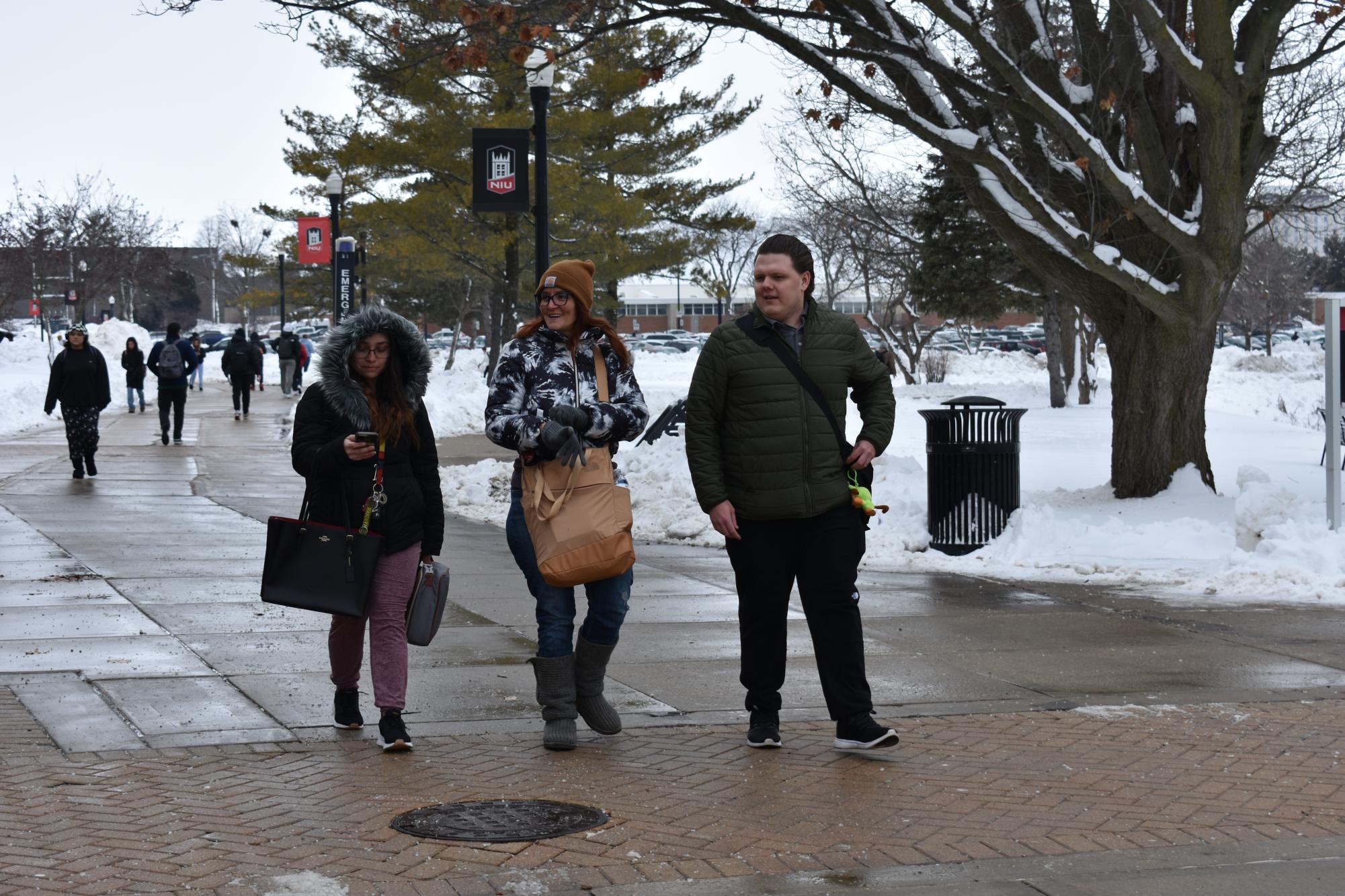 Junior special education majors Desiree Hancock (from left), Alix Sommers and Nicholas Hays talk as they walk past Cole Hall. The trio spent time discussing Arizona to help avoid thinking about the cold. (Nick Glover | Northern Star)
