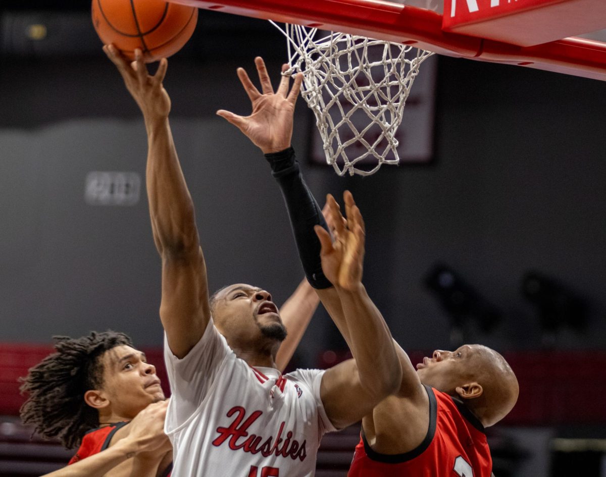 Sophomore forward Ethan Butler (15) goes for a layup as Ball State players reach toward him in defense. Butler contributed 7 points to the Huskies’ final score of 63 points for the game against the Cardinals. (Tim Dodge | Northern Star)