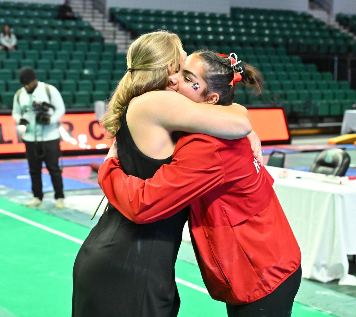 NIU senior gymnast Alyssa Al-Ashari hugs Eastern Michigan University gymnastics head coach Katie Minasola after Sundays MAC meet at the George Gervin GameAbove Center in Ypsilanti, Michigan. Al-Ashari, a native of Lansing, Michigan, competed in her home state for the final time, earning second-place finishes on bars and beam. (Steve King | EMU Athletics)