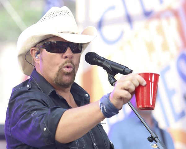 Toby Keith holds up a red Solo cup while standing in front of a microphone during a 2019 performance. Keith, known for his song Red Solo Cup, died on Feb. 5. (Photo by Greg Allen/Invision/AP, File)