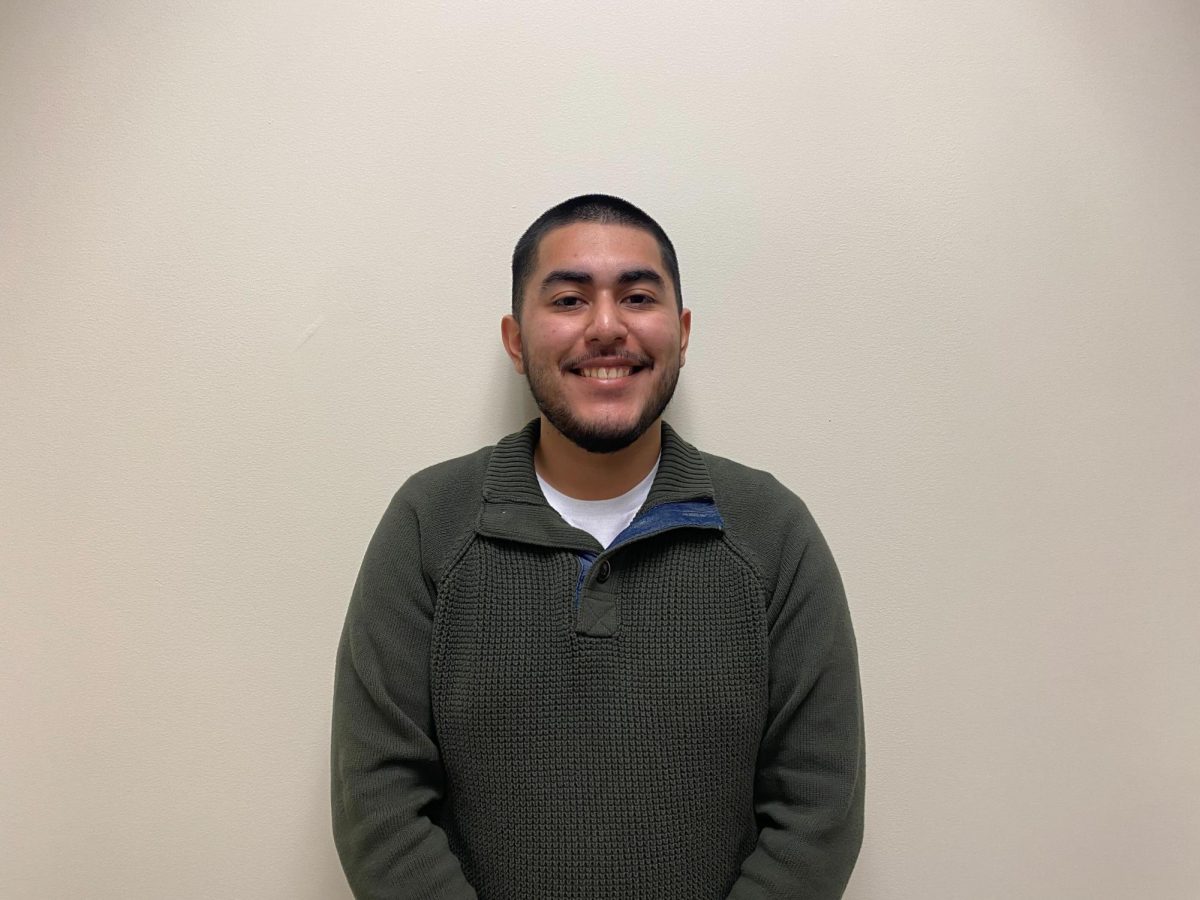 Gino Chavez, a senior marketing major, stands and smiles in a green sweater. Chavez was the winner of the Northern Stars Big Game contest. (Angelina Padilla-Tompkins | Northern Star)