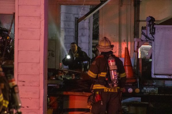 Two firefighters talk through the building’s garage Tuesday at 1031 W. Lincoln Highway. The spray from a hose damaged a hanging light fixture while crews attempted to suppress the fire from within the building. (Sean Reed | Northern Star)