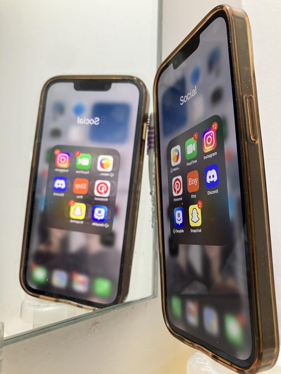 A phone with multiple social media apps is reflected in a mirror. Social media is only a reflection of real life, and users should be wary of misrepresentation. (Photo Illustration | Northern Star)
