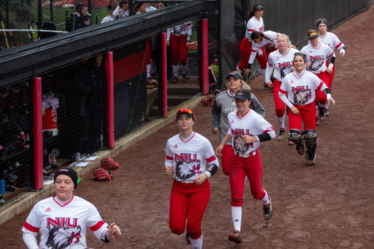 The NIU softball team runs out from the dugout after the NIU batter lineup was announced. The first home game saw a periodic cold drizzle until the last out of the final inning Tuesday, when the rain picked up substantially. (Totus Tuus Keely | Northern Star)
