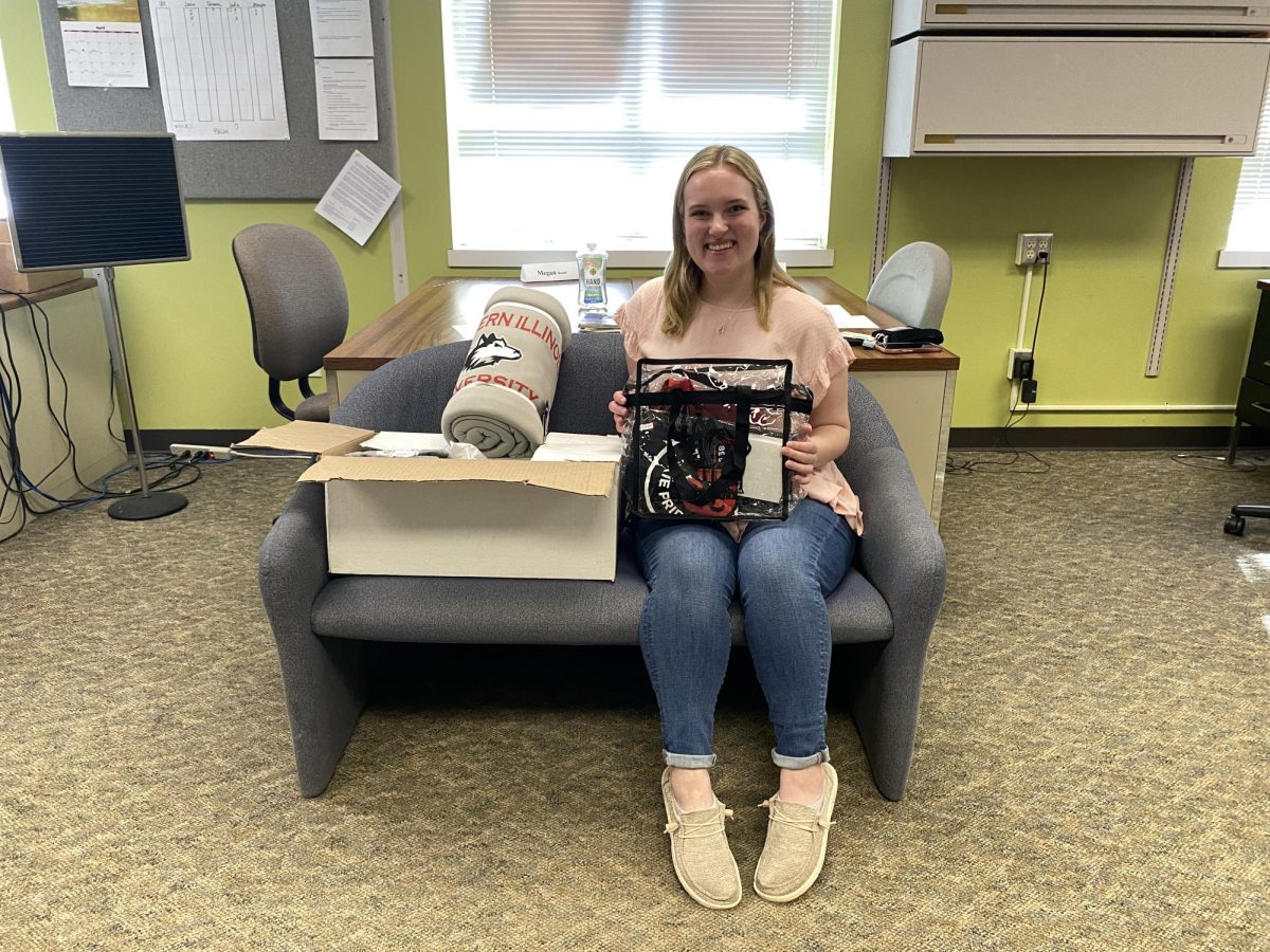 Caroline Menzer, a junior political science major, sits in the Northern Star office holding prizes donated by NIU and local businesses, valued just under $600, after locating the Northern Star Treasure Hunt paperweight Wednesday morning. (Sean Reed | Northern Star)
