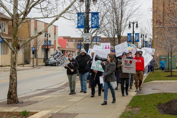 Kelsey Gettle, legal program manager for Safe Passage, leads a group of people in a rally. Tuesday evening Take Back the Night marched around the Egyptian Theater in honor of Sexual Assault Awareness month. (Sean Reed | Northern Star)