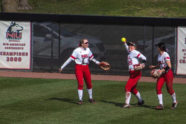 Sophomore right fielder Fiona Crane (26) throws the ball infield after catching the foul against the fence line in right field while senior center fielder Ellis Erickson (23) and junior second baseman Jenna Turner (4) cheer her on in the field. NIU softball was defeated 9-3 by the University at Buffalo Bulls Sunday. (Totus Tuus Keely | Northern Star)